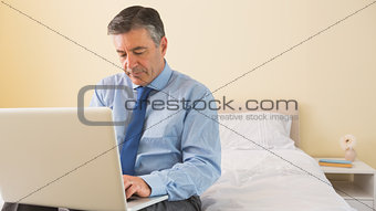 Thoughtfulman using a laptop sitting on a bed