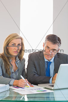 Two focused business people looking at camera trying to understand figures