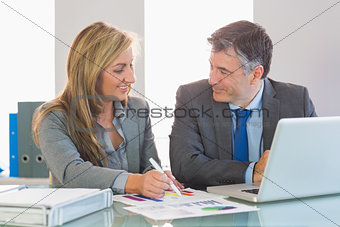 Two happy business people smiling to each other trying to understand figures