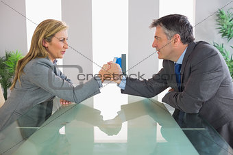 Two irritated businesspeople having an arm wrestling sitting around a table