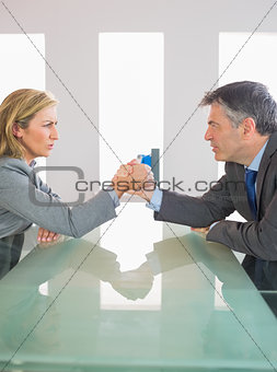 Two annoyed businesspeople having an arm wrestling sitting around a table