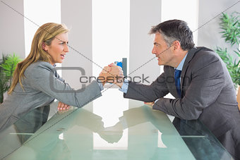 Two upset businesspeople having an arm wrestling sitting around a table