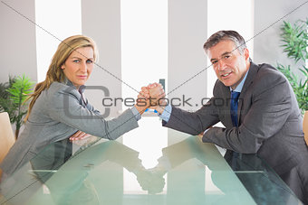 Two serious businesspeople having an arm wrestling sitting around a table
