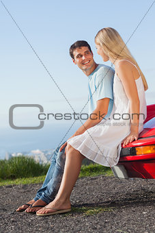 Smiling couple sitting on their cabriolet car hood