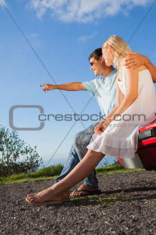Cheerful cute couple sitting on their cabriolet car hood