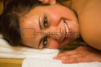 Happy brunette lying in a sauna looking at camera