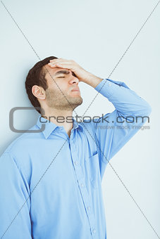 Upset man eyes closed and a hand on the forehead leaning against a wall