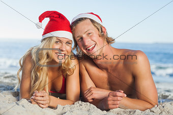 Couple lying on beach wearing christmas hats