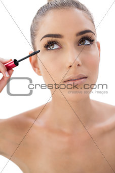 Pensive woman applying mascara