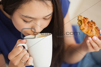 Young asian woman sipping her coffee and holding a pastry