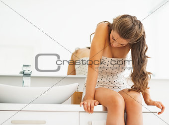 Frustrated young woman sitting in bathroom