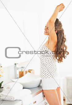 Young woman in bathroom stretching after sleep