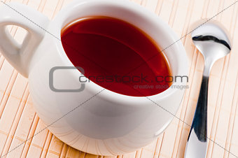 White cup with fresh tea on wooden mat.