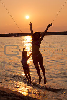 Lady and little girl jumping on the beach enjoying summer