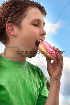 Boy biting a yummy pink iced doughnut (donut)