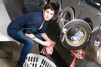 Serious Woman Does Chores Folding Clothes in the Laundromat