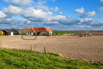 tractor plowing field by farmhouse
