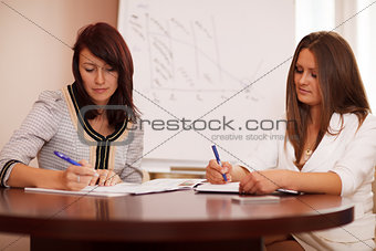 Two women taking notes at a business presentation