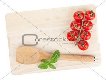 Cooking utensil and tomato with basil over cutting board