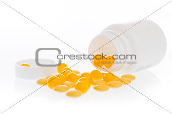 Yellow pills scattered in front of the white plastic jar.