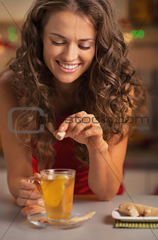 Smiling young woman adding cane sugar cube in ginger tea