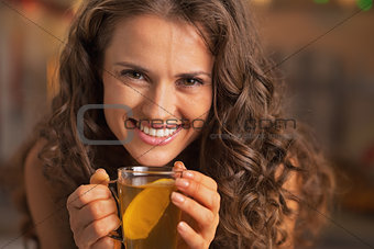 Smiling young woman drinking ginger tea with lemon
