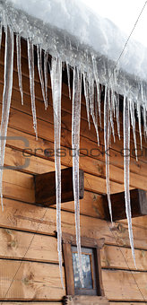 Wooden house with big icicles on snow-covered roof