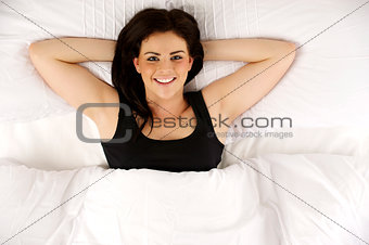 Woman laid in bed relaxed looking up at the camera smiling