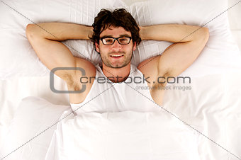 Man laid in white bed looking up at the camera smiling