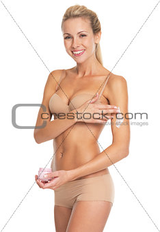 Happy young woman in lingerie applying creme on arm
