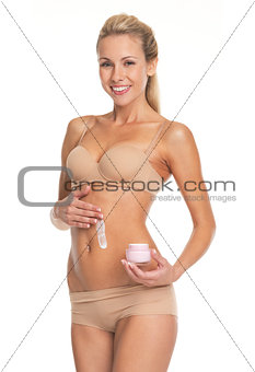 Happy young woman in lingerie applying creme on belly