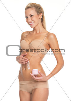 Smiling young woman in lingerie applying creme on belly