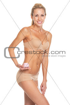 Happy young woman in lingerie applying creme on leg