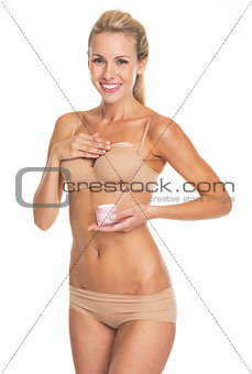 Happy young woman in lingerie applying creme on breast