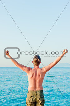 a man with a naked torso is by the sea and put his hands up at dawn