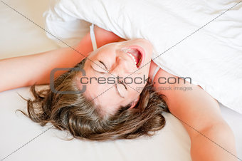 girl in a white bed yawns and stretches in the morning