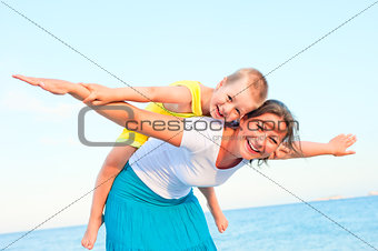mother and son sitting on her back, happy playing on the beach