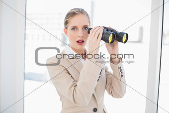 Shocked blonde businesswoman holding binoculars