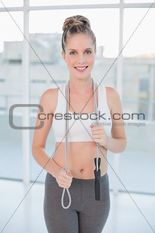 Smiling sporty blonde holding skipping rope around neck