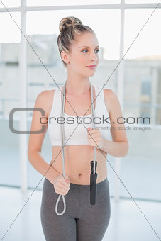 Pensive sporty blonde holding skipping rope around neck