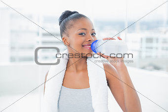 Fit woman with towel around her neck drinking water while looking at camera
