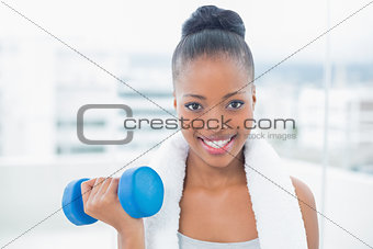 Smiling woman with towel around her neck working out with dumbbell