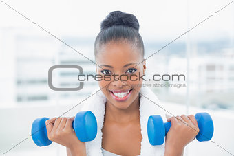 Fit woman with towel around her neck working out with dumbbell