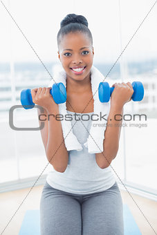 Fit smiling woman with towel around her neck working out with dumbbell