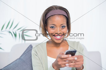 Cheerful elegant woman sitting on sofa text messaging