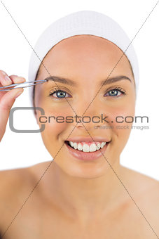 Smiling woman wearing headband using tweezers