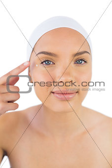 Attractive woman weaing headband putting cream on her face