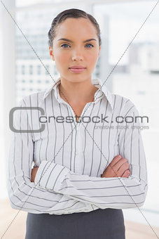 Serious businesswoman standing in an office crossing arms