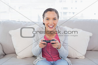 Smiling woman sitting on sofa playing video games