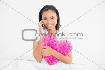 Smiling young dark haired model holding a pillow and making a phone call